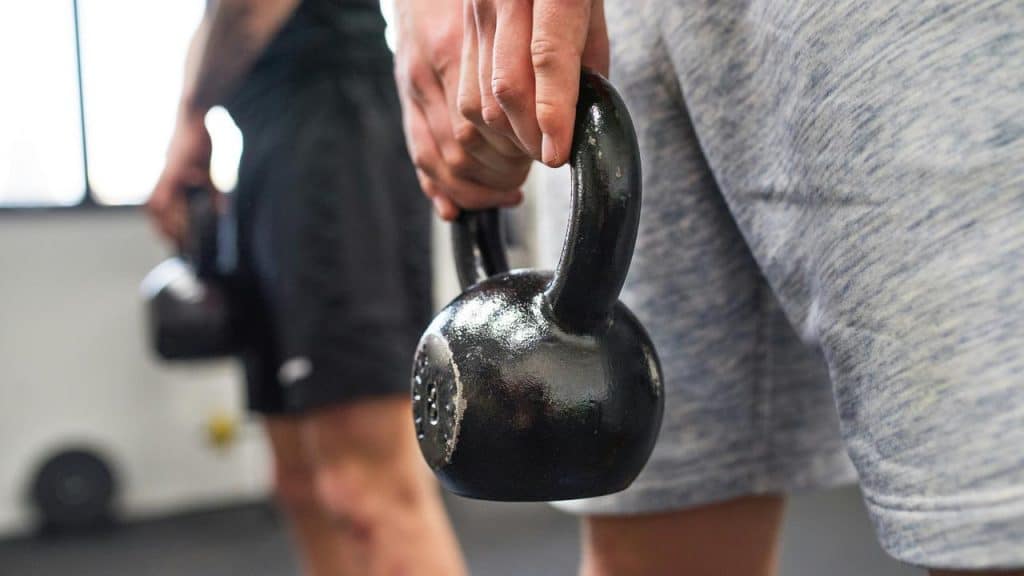 A person holding a kettlebell at their side in a gym.