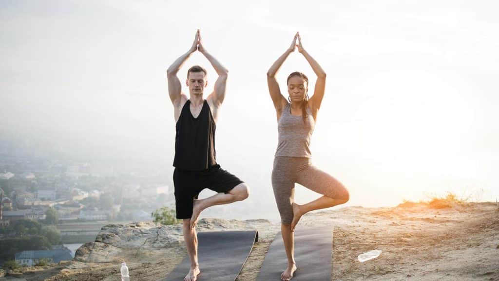 A man and woman doing tree pose on yoga mats overlooking a city.
