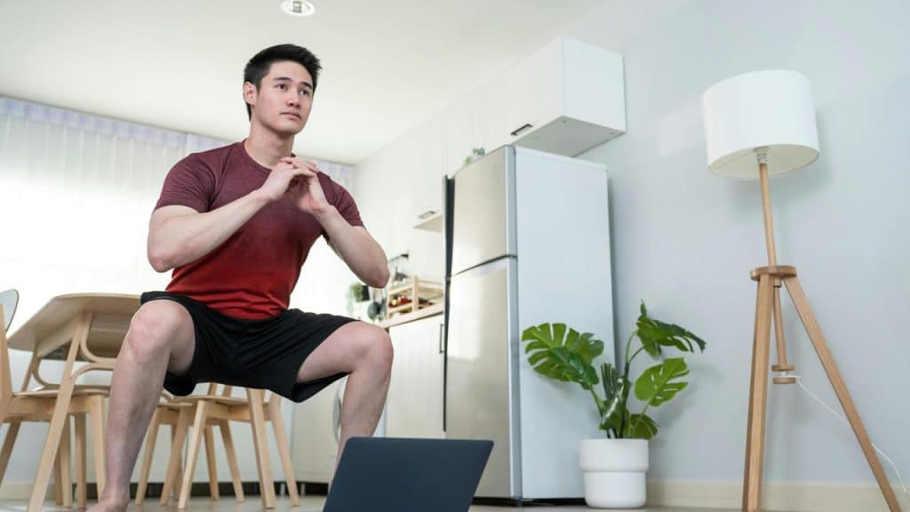 A man squatting in front of a laptop at home.