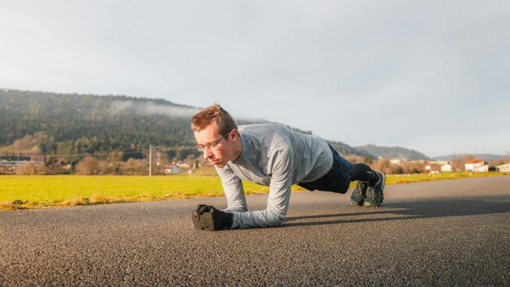 A man holding a forearm plank on a rural road.