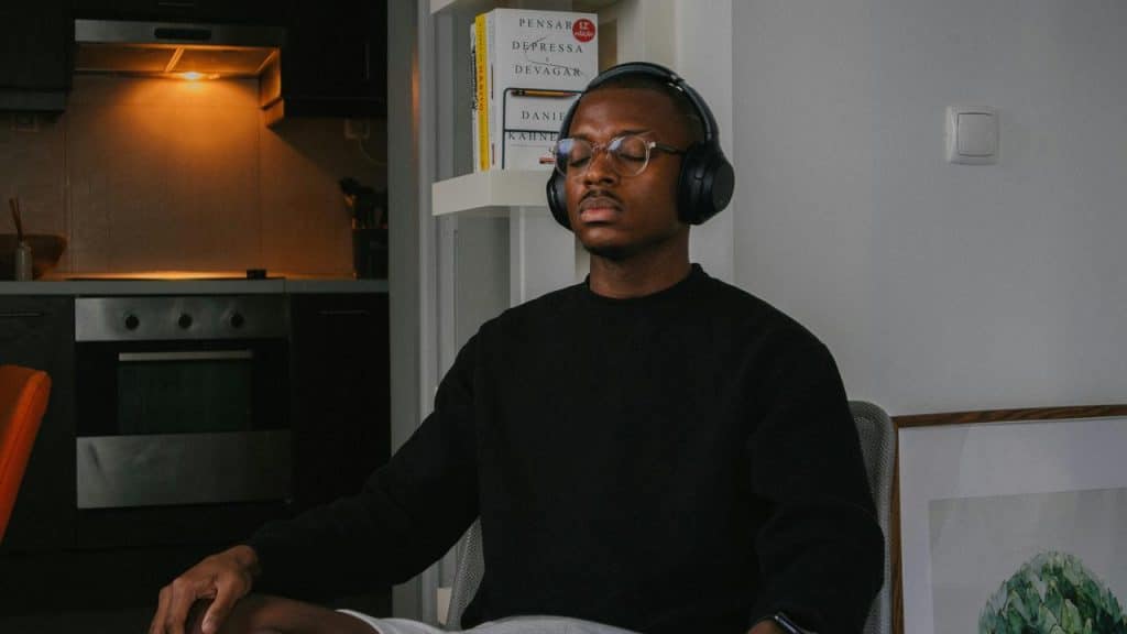 A man wearing headphones with his eyes closed sitting in a kitchen.