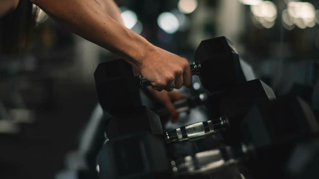 A hand gripping a dumbbell’s handle on a gym rack.