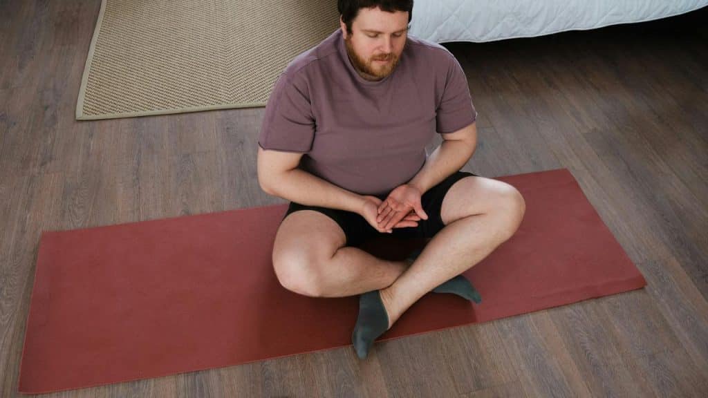 A man meditating cross-legged on a yoga mat.