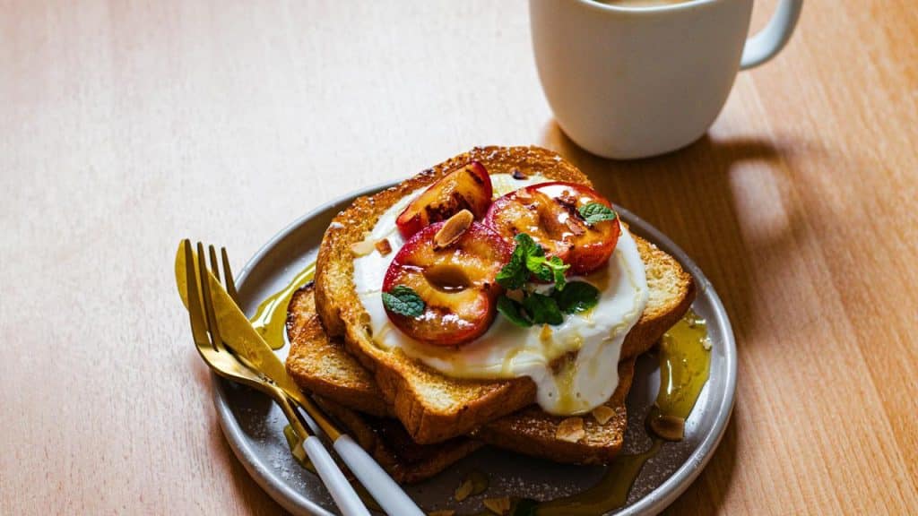 A stack of toast with cream, roasted plums, mint, and honey.