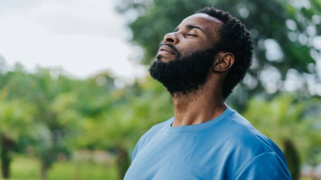 A bearded man in a blue shirt outdoors with his eyes closed.