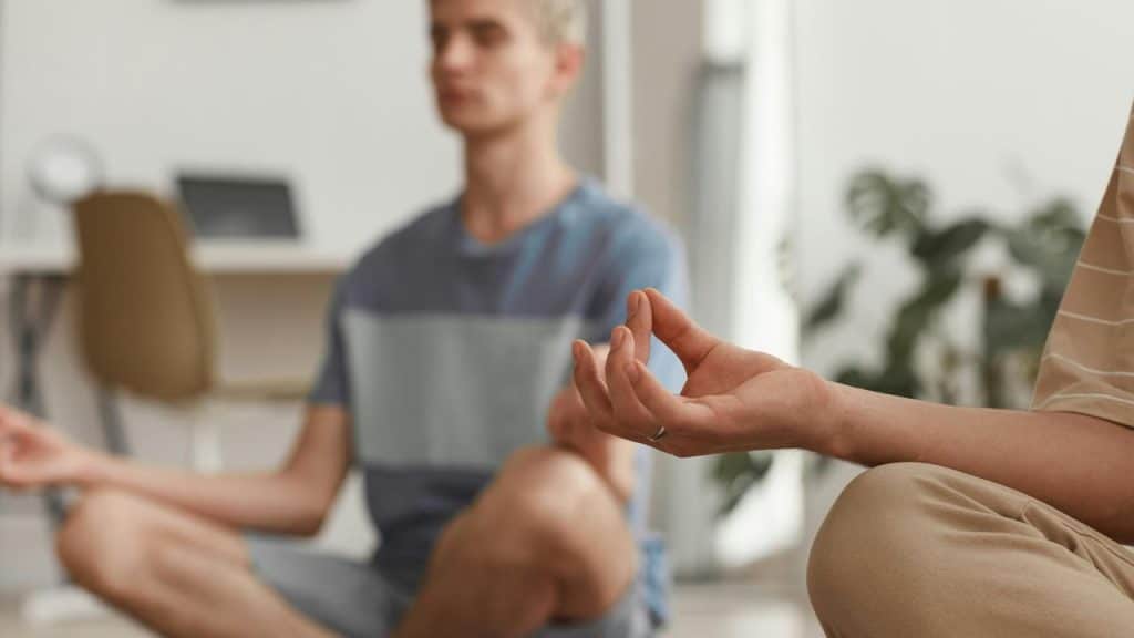 A pair of cross-legged people meditating indoors.