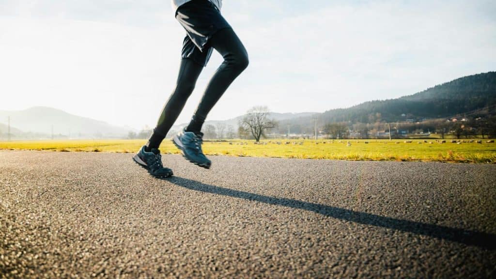 A runner’s legs in motion on a paved country road.