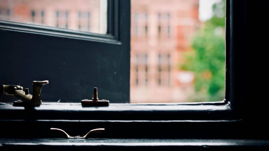 A metal window latch on a dark frame with a blurred building outside.