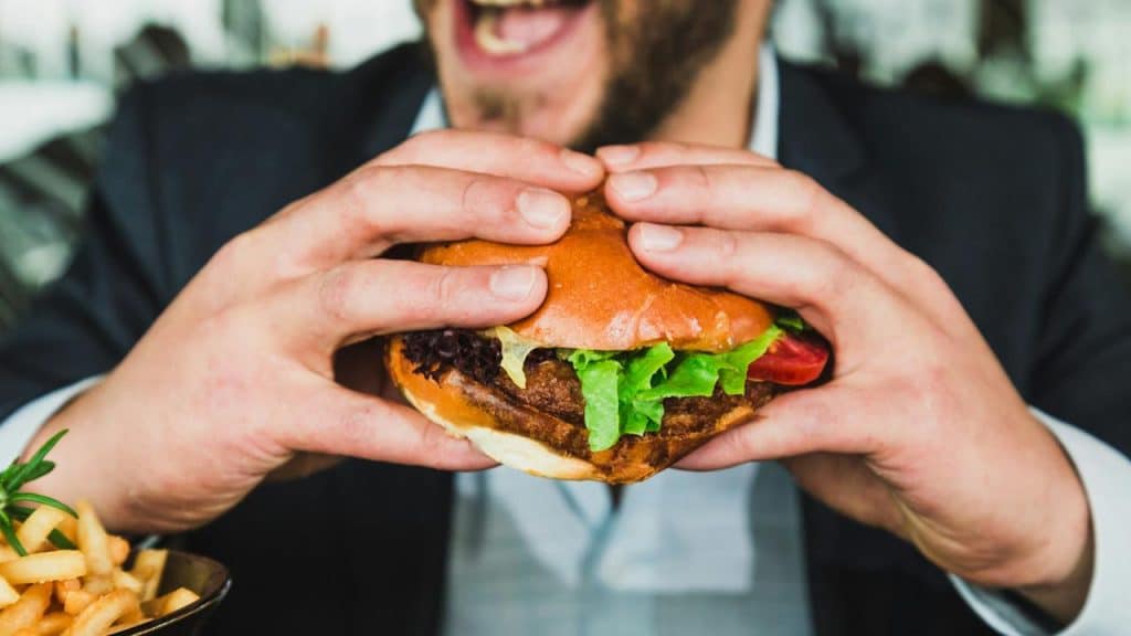 A man holding a lettuce-topped burger before taking a bite.