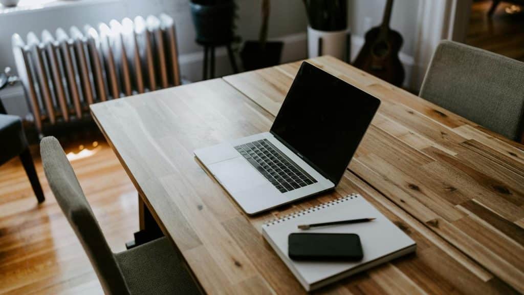An open laptop beside a notebook, pencil, and smartphone on a wooden table.