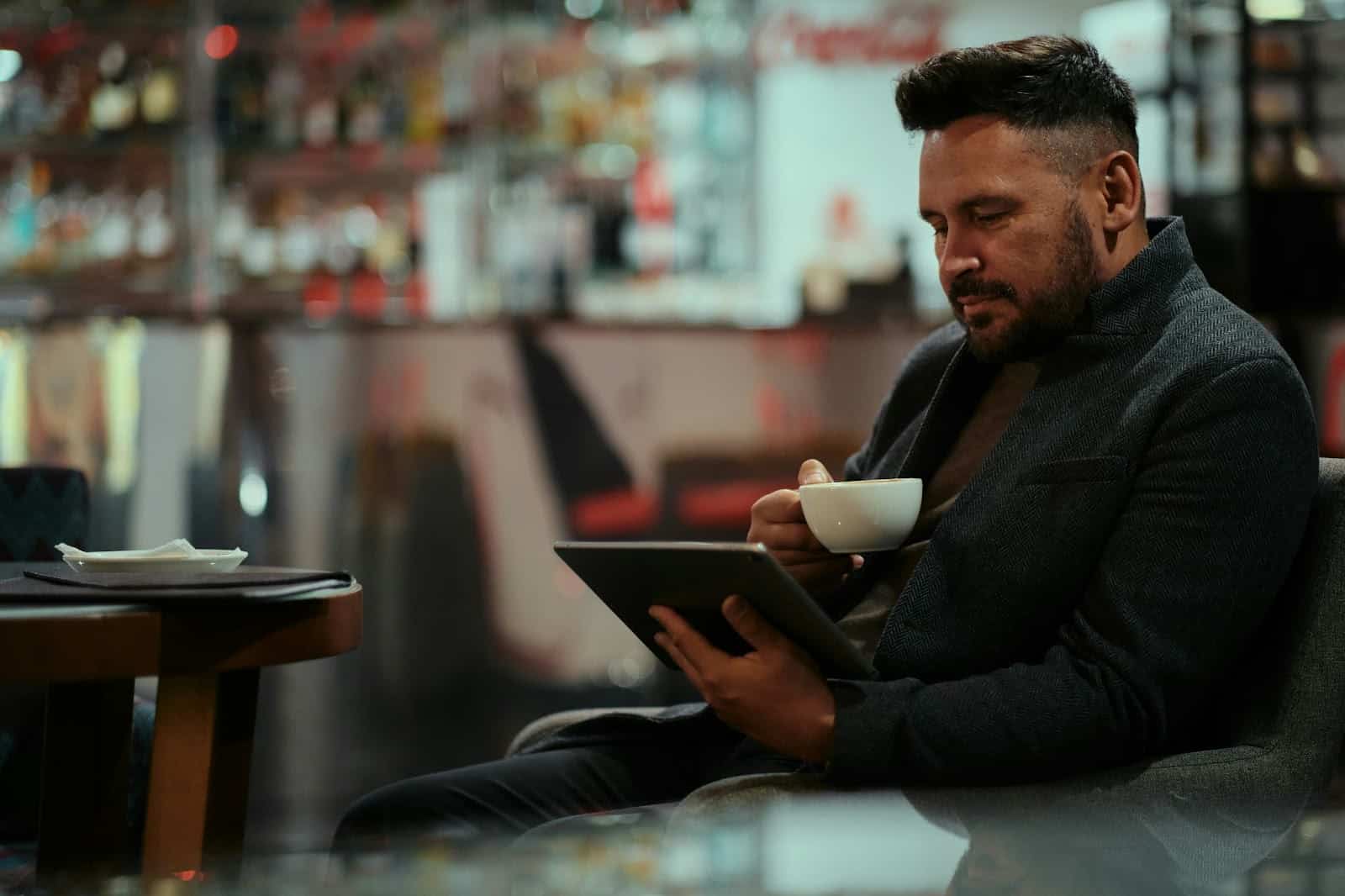 A picture of a man using a tablet while drinking coffee.