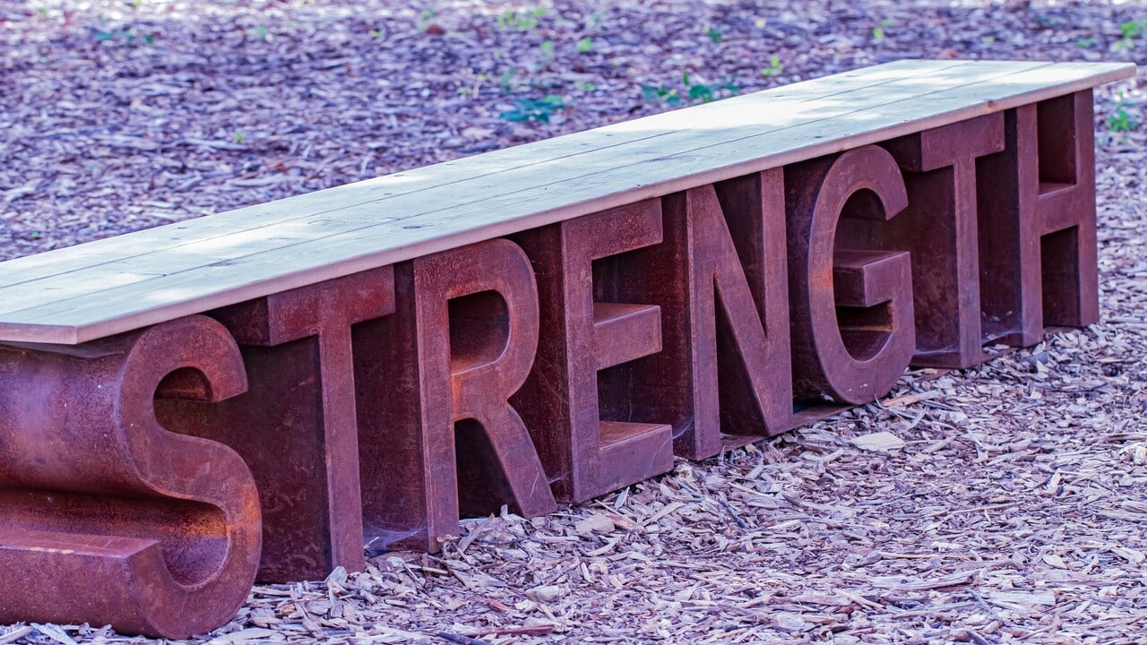 A bench on the ground spelling out “strength”.