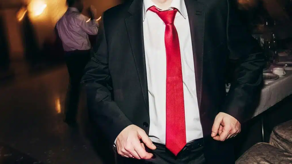 A man in a dark suit and bright red tie standing indoors at a formal event.