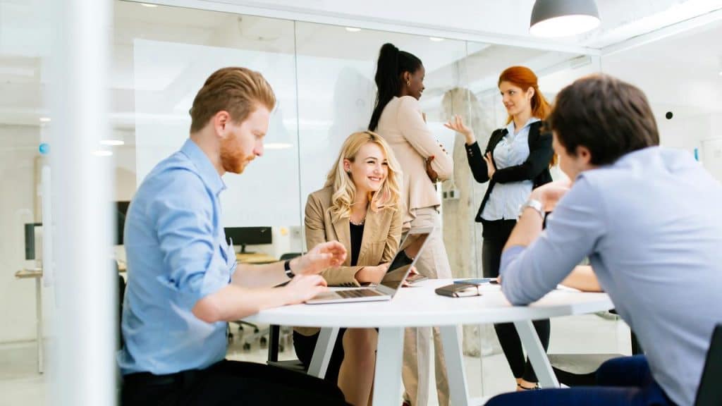 A diverse group of coworkers collaborating around a round table in a bright, modern office.