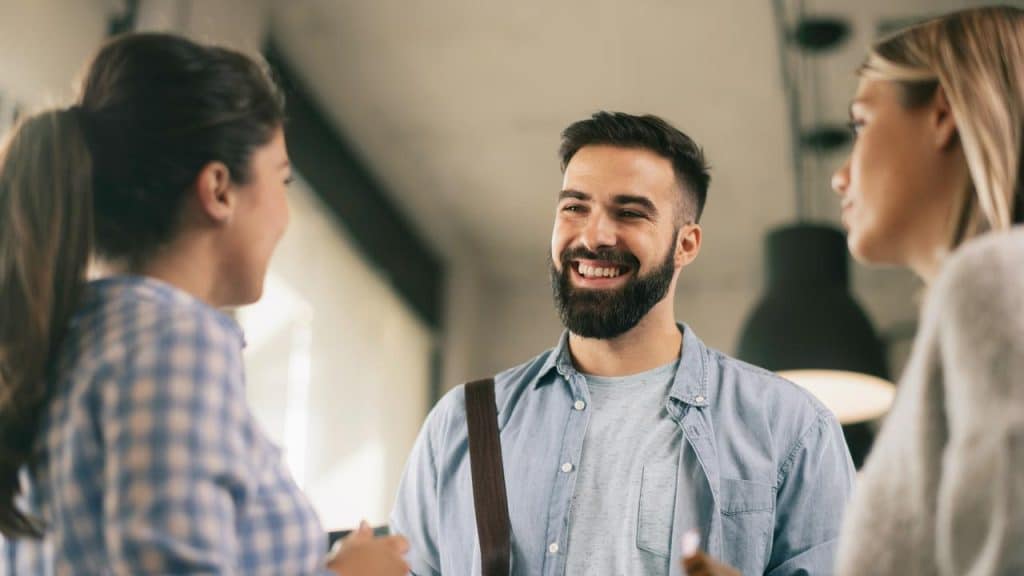 A bearded man smiling while chatting with two women.
