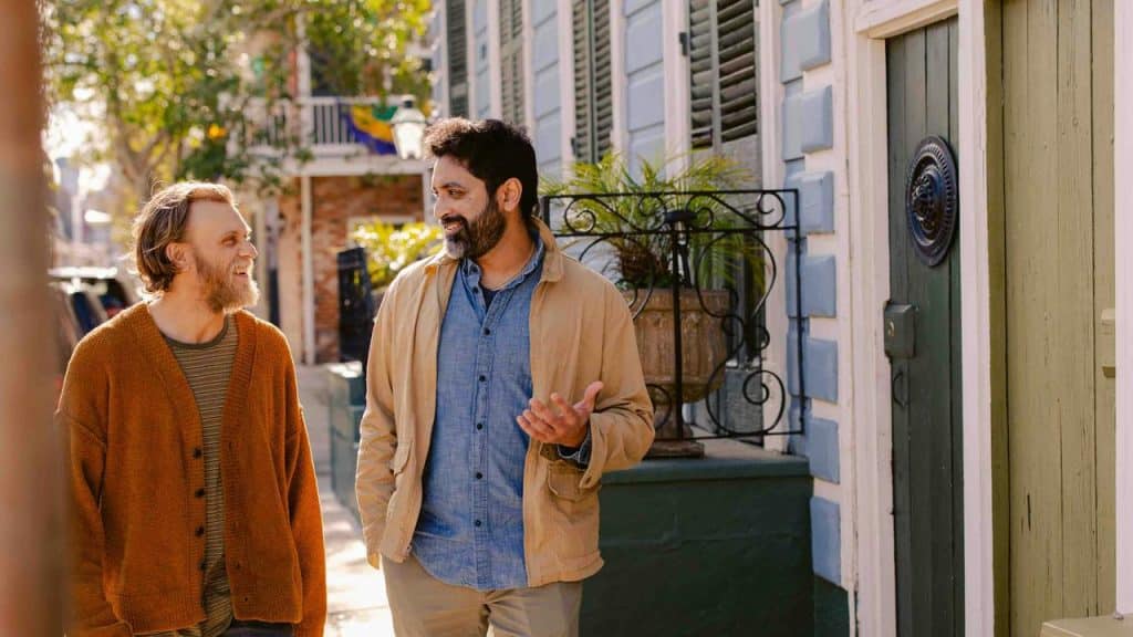 A pair of men strolling and chatting along a sunlit residential street.