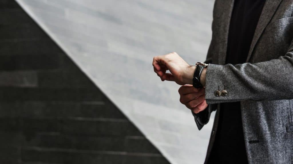 A person in a grey blazer adjusting a wristwatch.