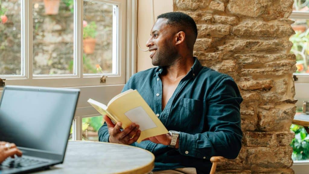 A man holding a book and smiling as he looks out a window.