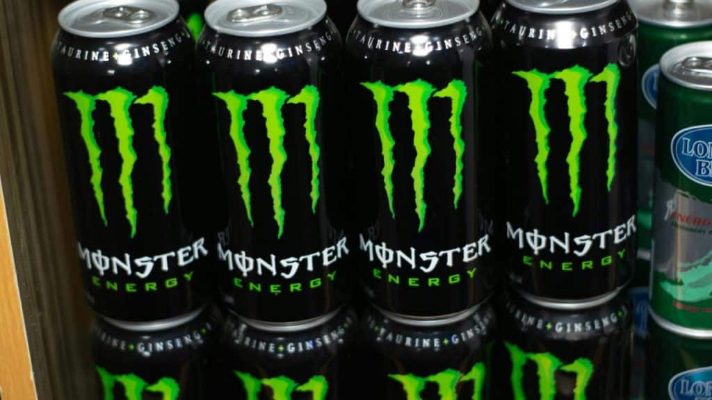 A row of black Monster Energy drink cans emblazoned with the neon green claw logo on a shelf.
