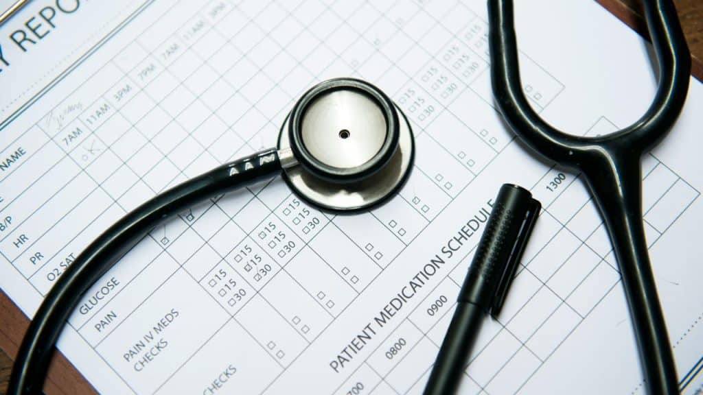 A stethoscope and black pen resting atop a printed patient medication schedule form with time-slot checkboxes.