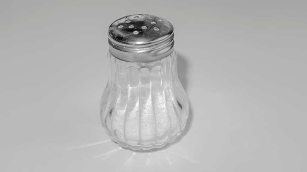 A glass salt shaker with a metal perforated lid on a white surface.