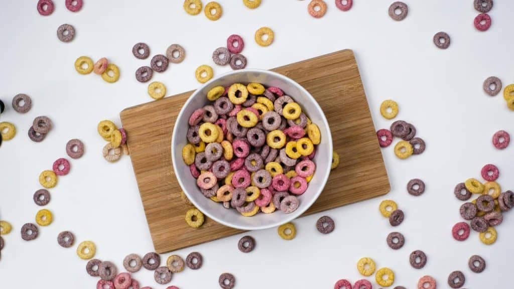 A bowl of colorful cereal rings on a wooden board with scattered pieces around.