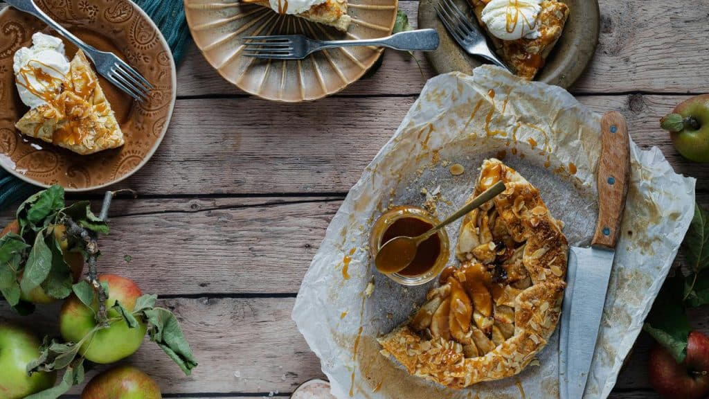 An apple galette drizzled with caramel and almonds alongside plated slices.
