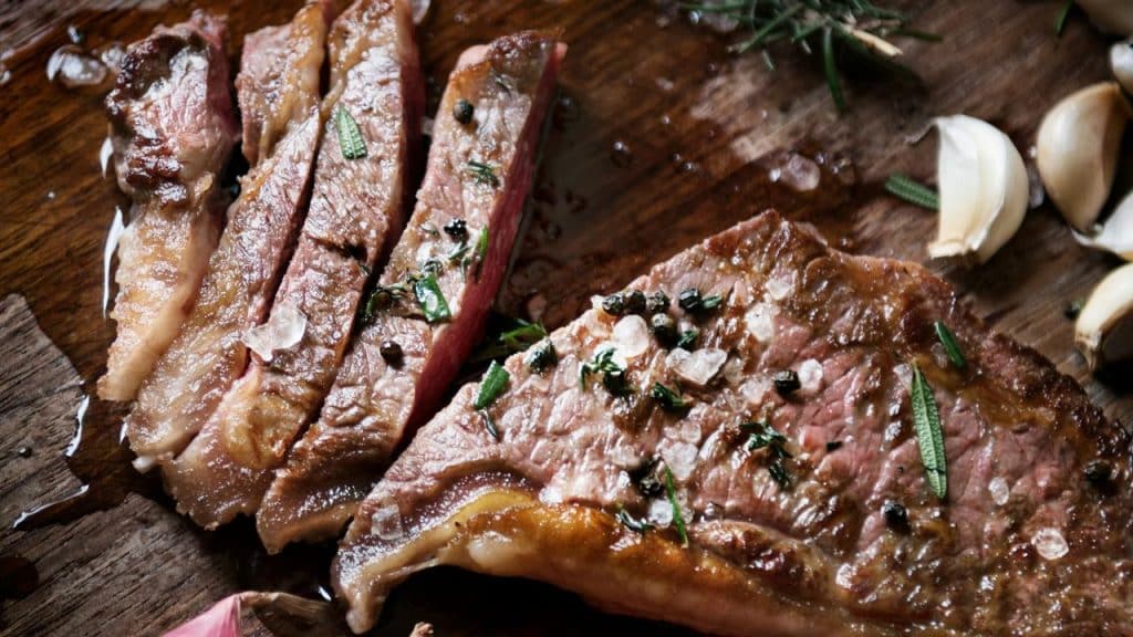A sliced medium-rare steak sprinkled with coarse salt and herbs on a wooden board.