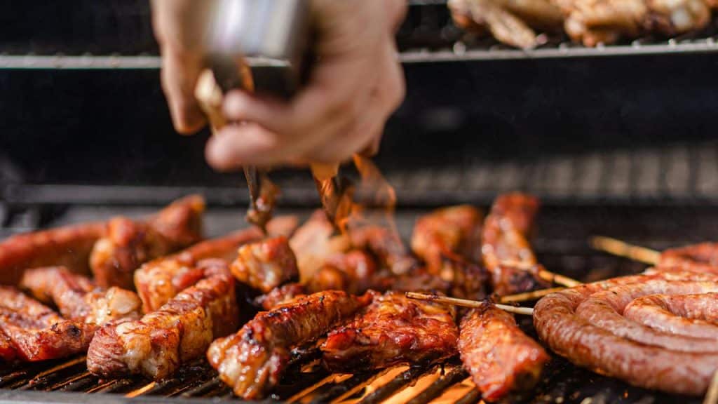 A barbecue grill with sausages and ribs being turned with tongs.