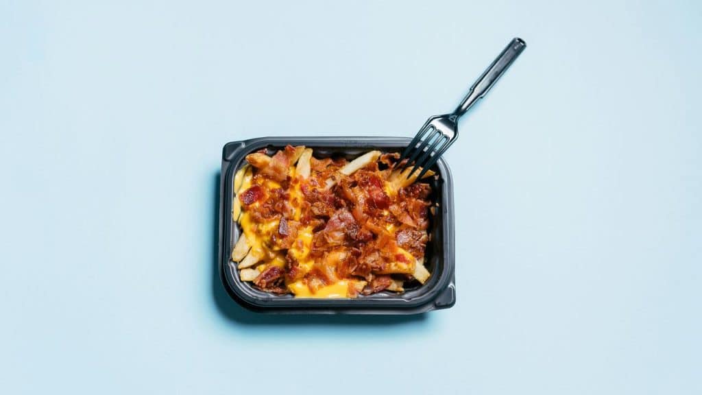 A container of cheese fries topped with bacon and a fork.