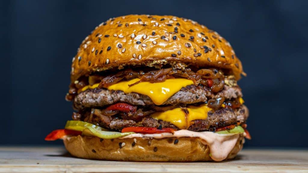 A double cheeseburger with melted cheese, caramelized onions, pickles, and sauce in a sesame seed bun.