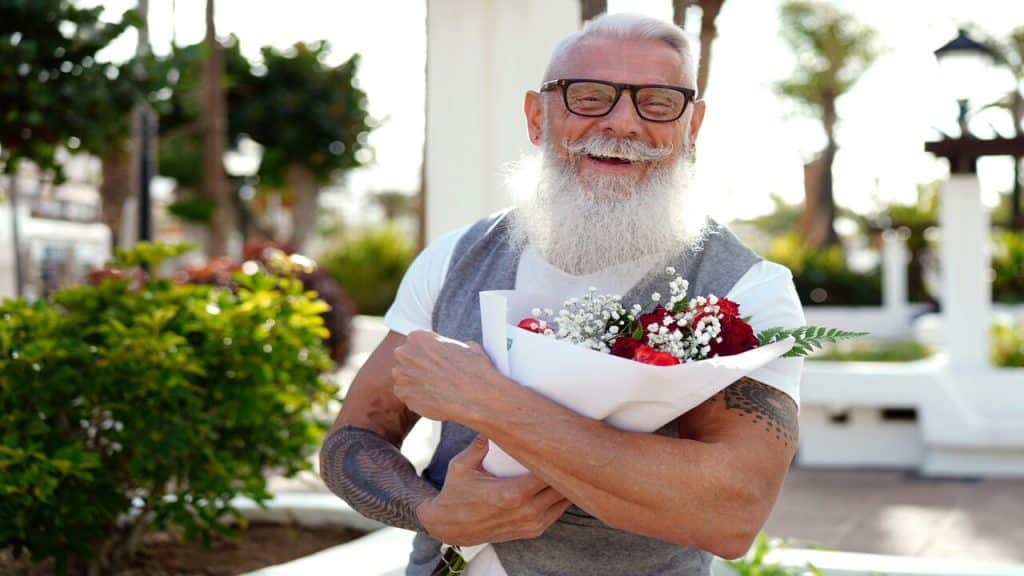 An older man smiling at the camera and holding flowers