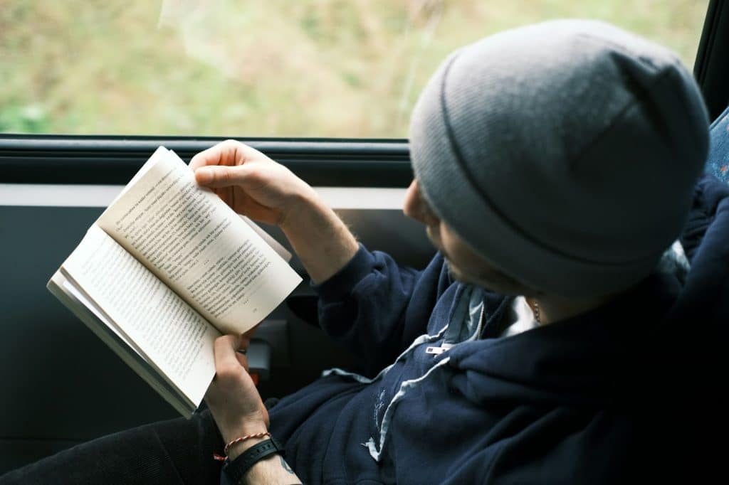 A man reading a book beside the window.