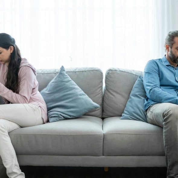 A man and a woman sit on opposite ends of a couch, looking away from each other.