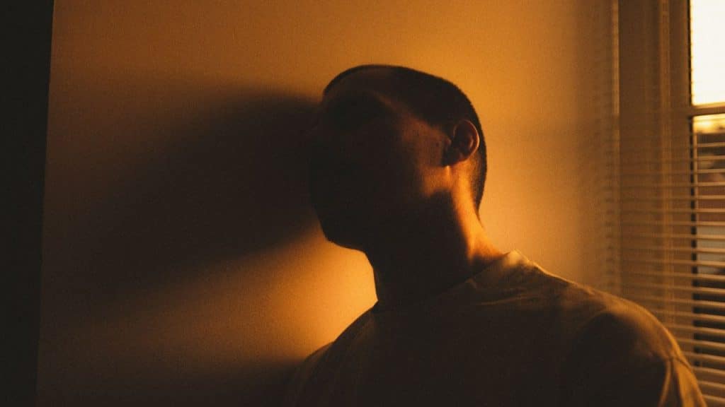 A man's silhouette is cast on a wall with orange light from a nearby window.
