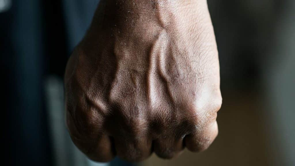 A close-up of a dark-skinned, veined fist with prominent knuckles.