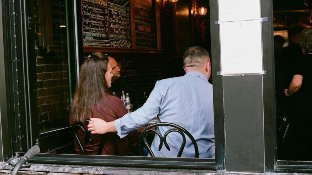 A man with his back to the camera has his arm around a woman, both seated at a restaurant table.