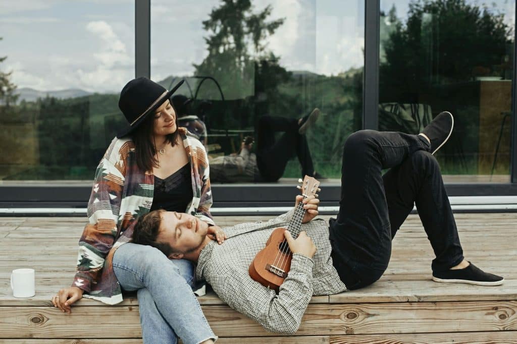 A man holding a ukulele while resting a woman’s lap