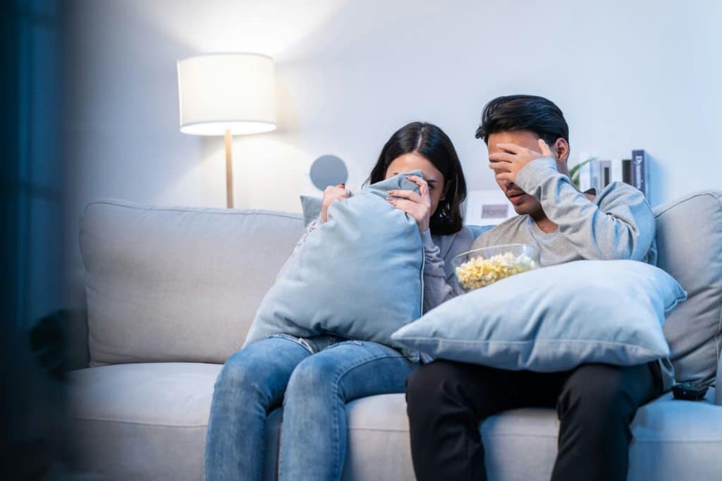 A man and woman covering their eyes because of a horror movie