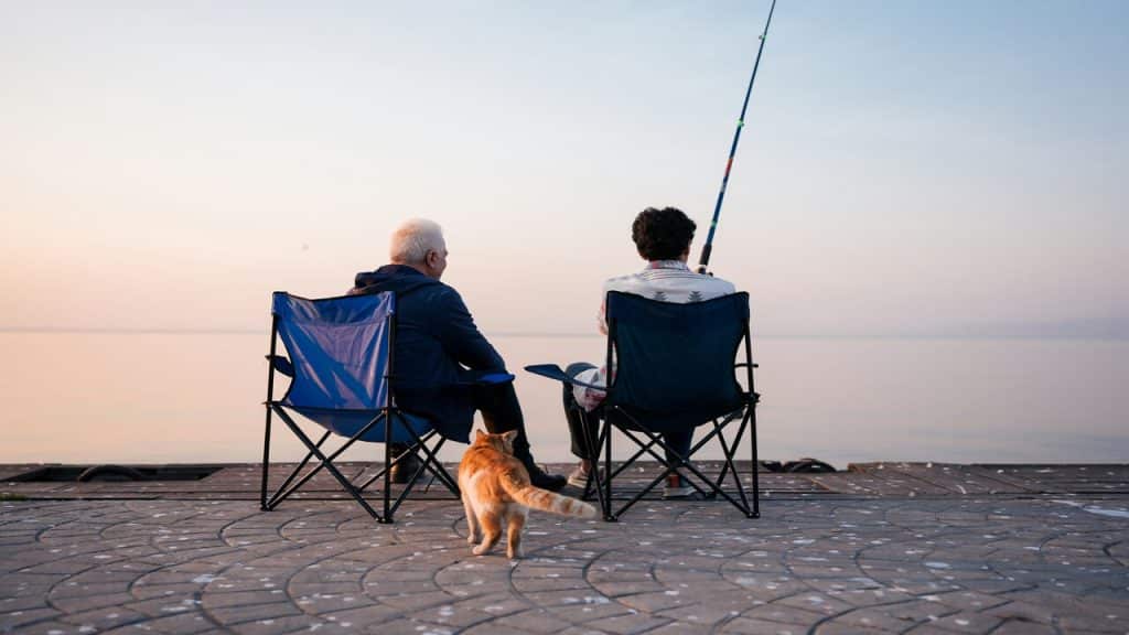 Two men sitting on lawn chairs fishing.