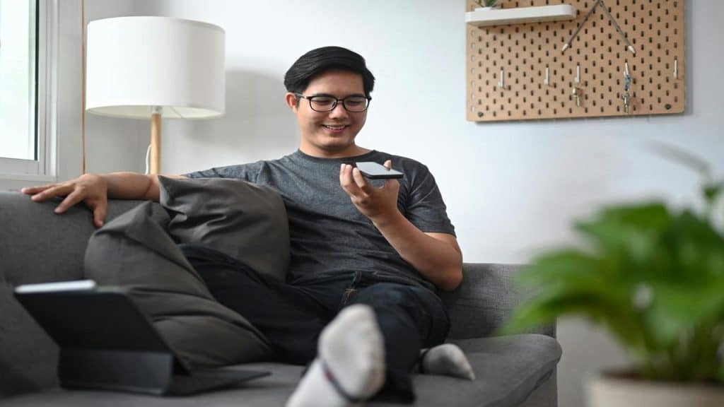 A man relaxing on a sofa using voice command on his smartphone.