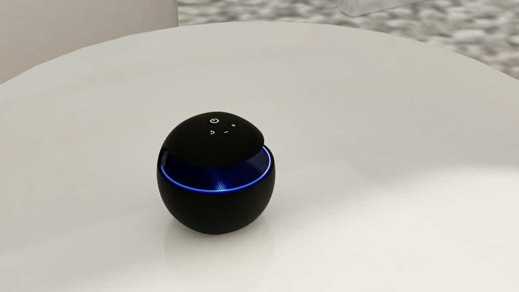 A round black Bluetooth speaker with blue LED lighting on a white table.