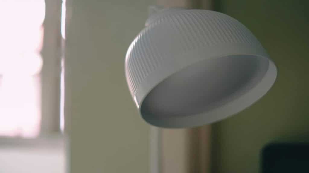 A close-up of a modern white desk lamp with a ribbed shade near a softly lit window.