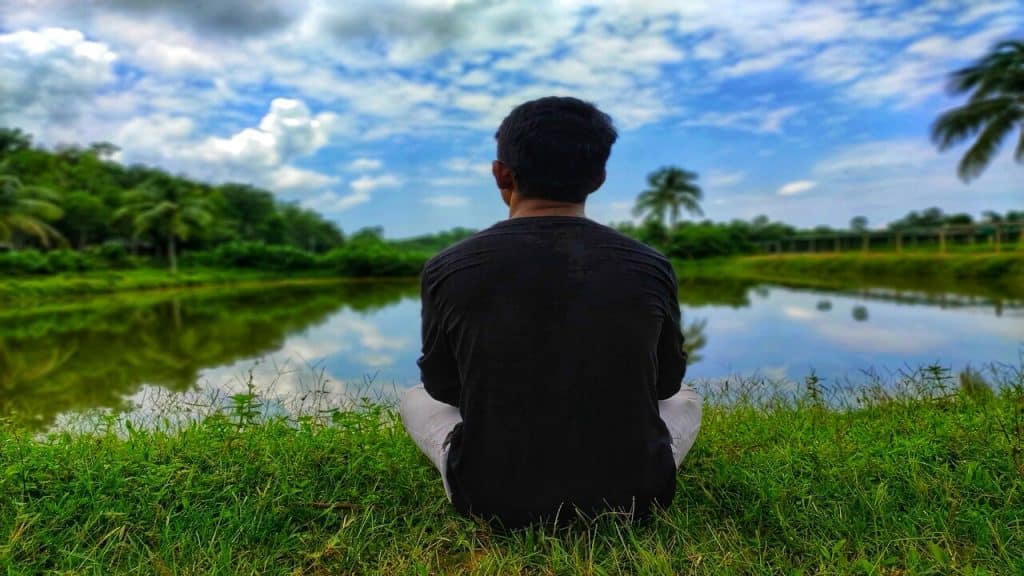 A man sitting on grass beside a lake.