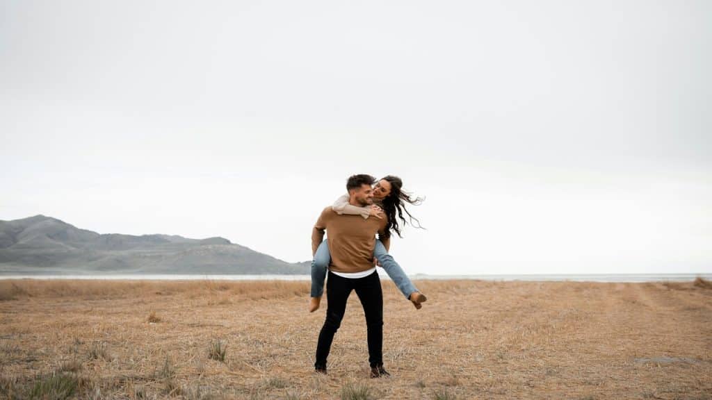 A woman piggy-backing on a man in a field.