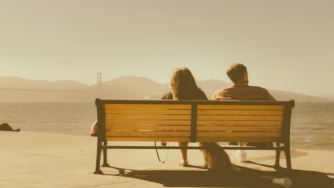 A couple sitting on a bench not looking at each other.