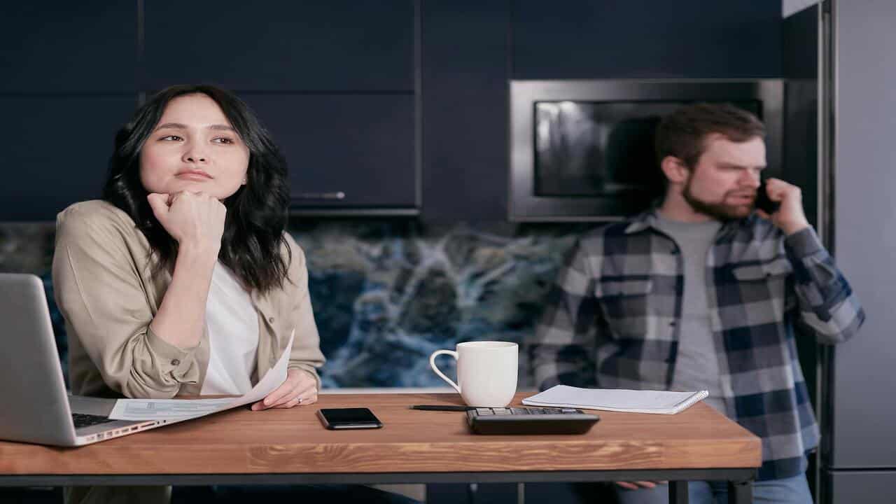 A woman looks pensive while her husband is on the phone.