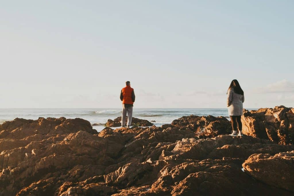 A man at looking at the view while a woman looking at him from afar.