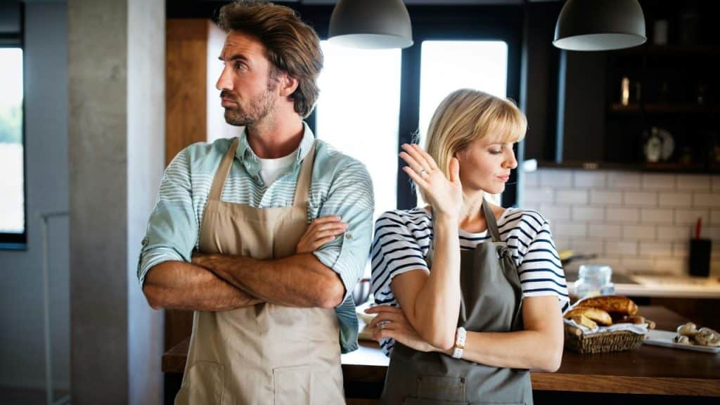 A man and woman, both wearing aprons, stand back-to-back with arms crossed.
