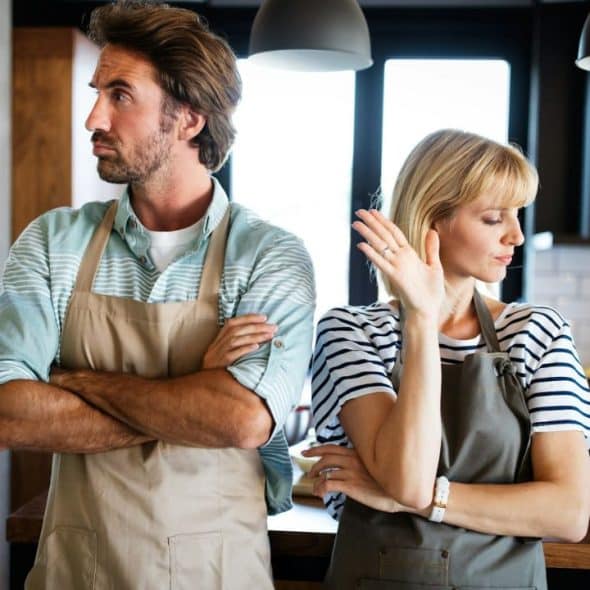 A man and woman, both wearing aprons, stand back-to-back with arms crossed.